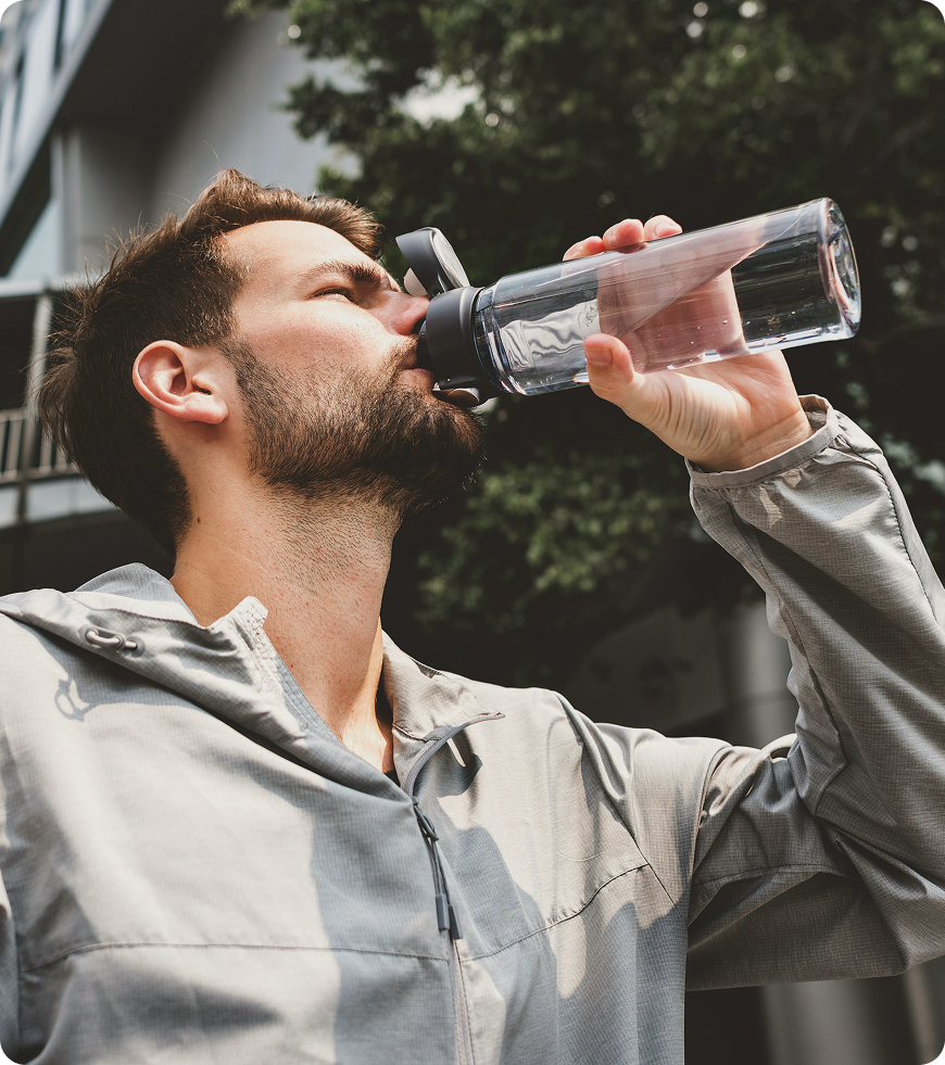 Man drinking water while standing on a city street, reflecting daily habits and hydration linked to lifestyle support from Tirzepatide in Des Moines