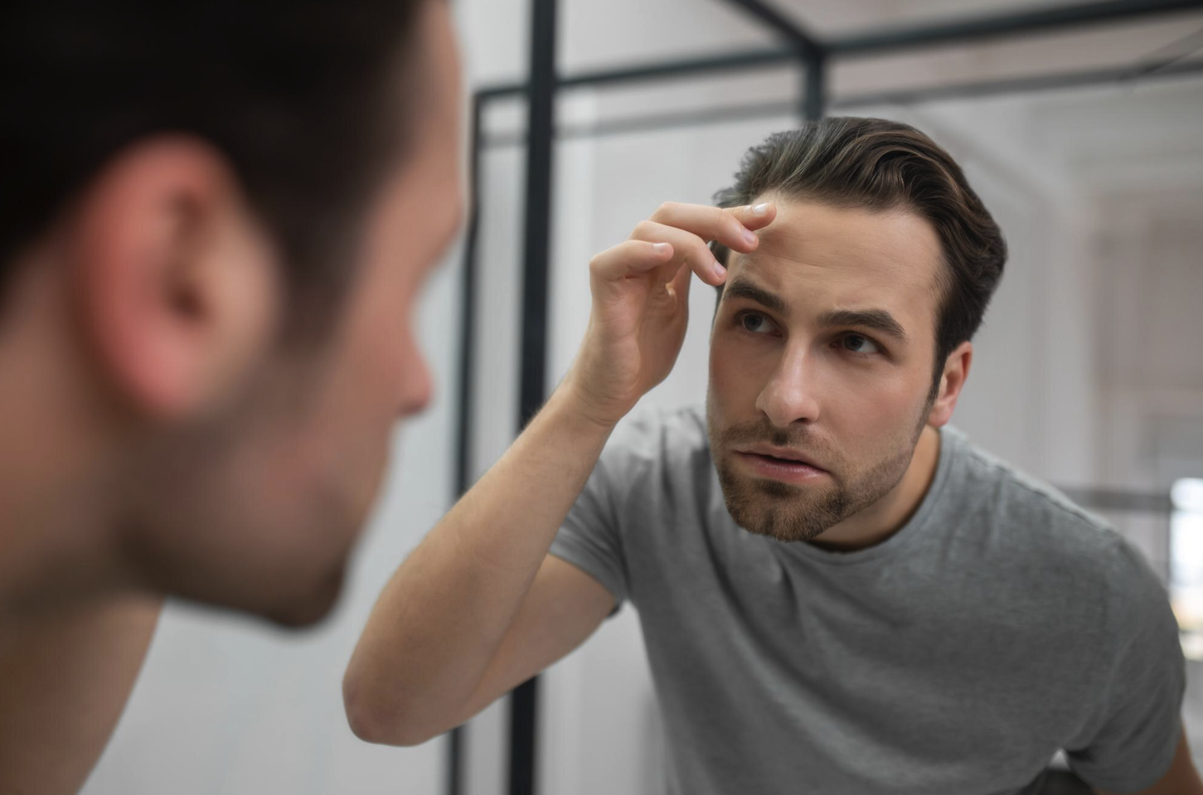 Man looking at his hair in the mirror, representing comparison between minoxidil vs finasteride treatments for hair loss and regrowth