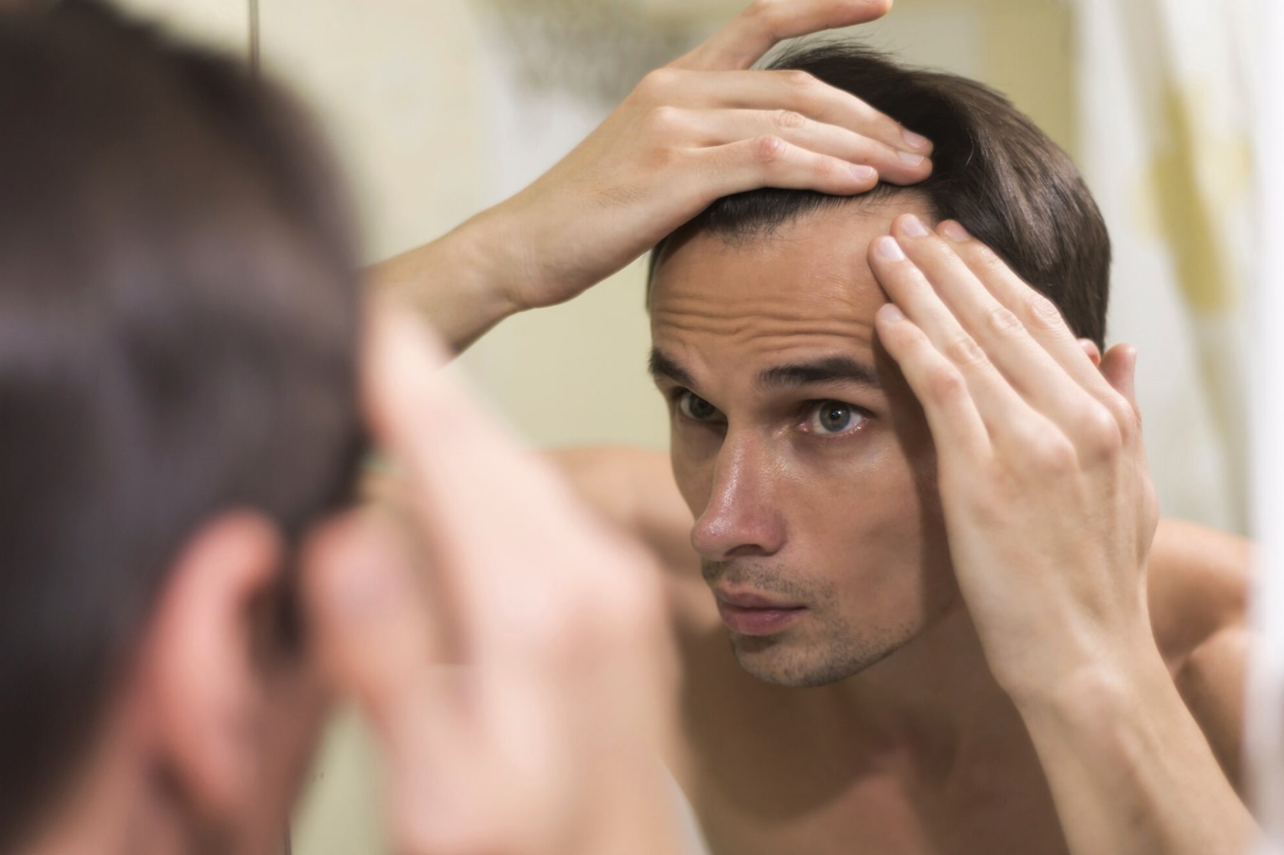 Man looking closely in the mirror as he notices early hair loss and thinning at the hairline.