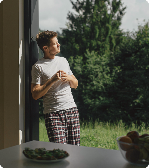 Man standing at home holding a cup of coffee while looking at the sunrise, reflecting daily balance and wellness supported by Thymosin Alpha-1 Peptide Injections in {{location_name}} at Gameday Men’s Health {{city}}