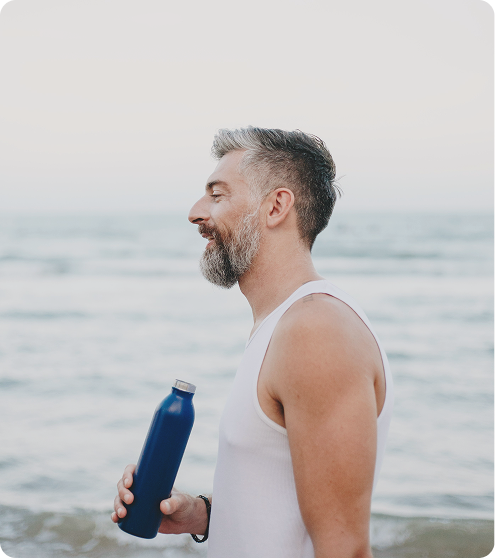 Man near the ocean staying hydrated, symbolizing daily wellness and routine associated with Epitalon Peptide Injections in {{location_name}}