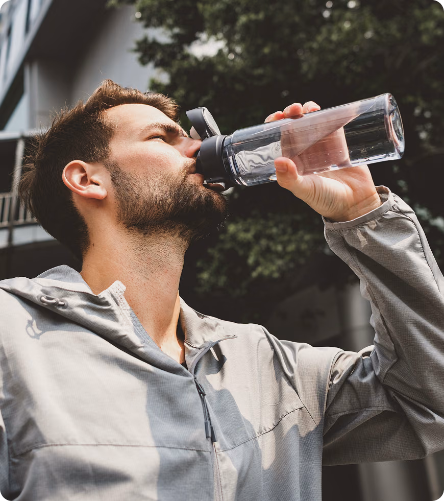 Man drinking water while standing on a city street, reflecting daily habits and hydration linked to lifestyle support from Tirzepatide in Missouri