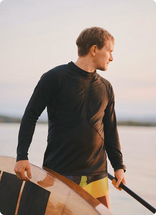Man standing on the beach with a paddleboard, representing balance, recovery, and wellness supported by Glutathione injections in Elmhurst, Illinois.