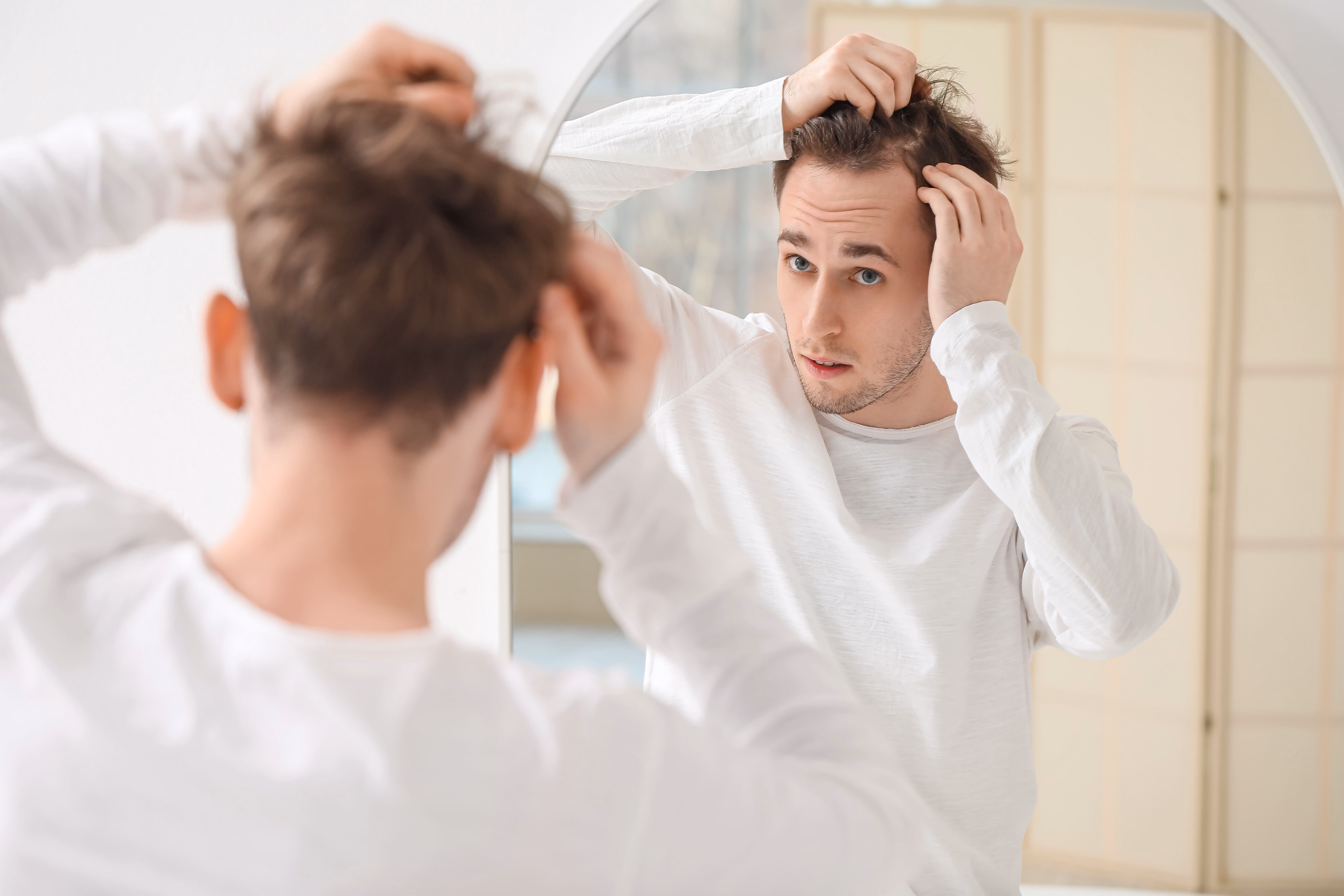 Man examining thinning hair in mirror at home