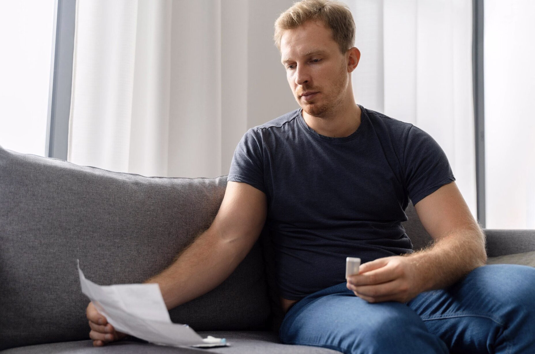 Thoughtful man sitting on a sofa reviewing paperwork, reflecting common signs of low testosterone such as fatigue, low motivation, and hormonal changes.
