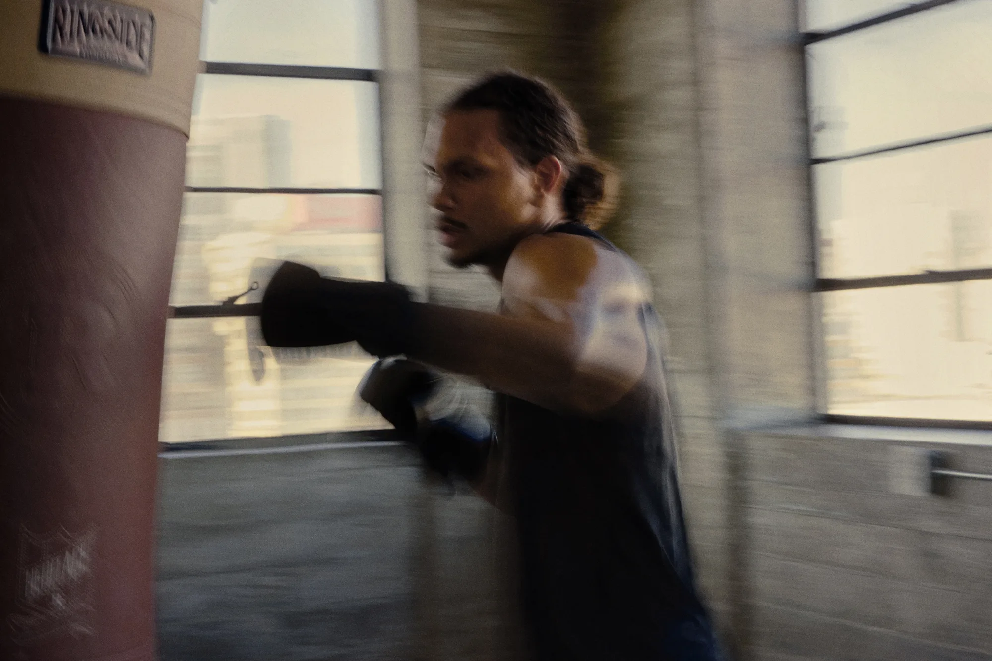 Man training with boxing gloves at a heavy bag in a sunlit gym