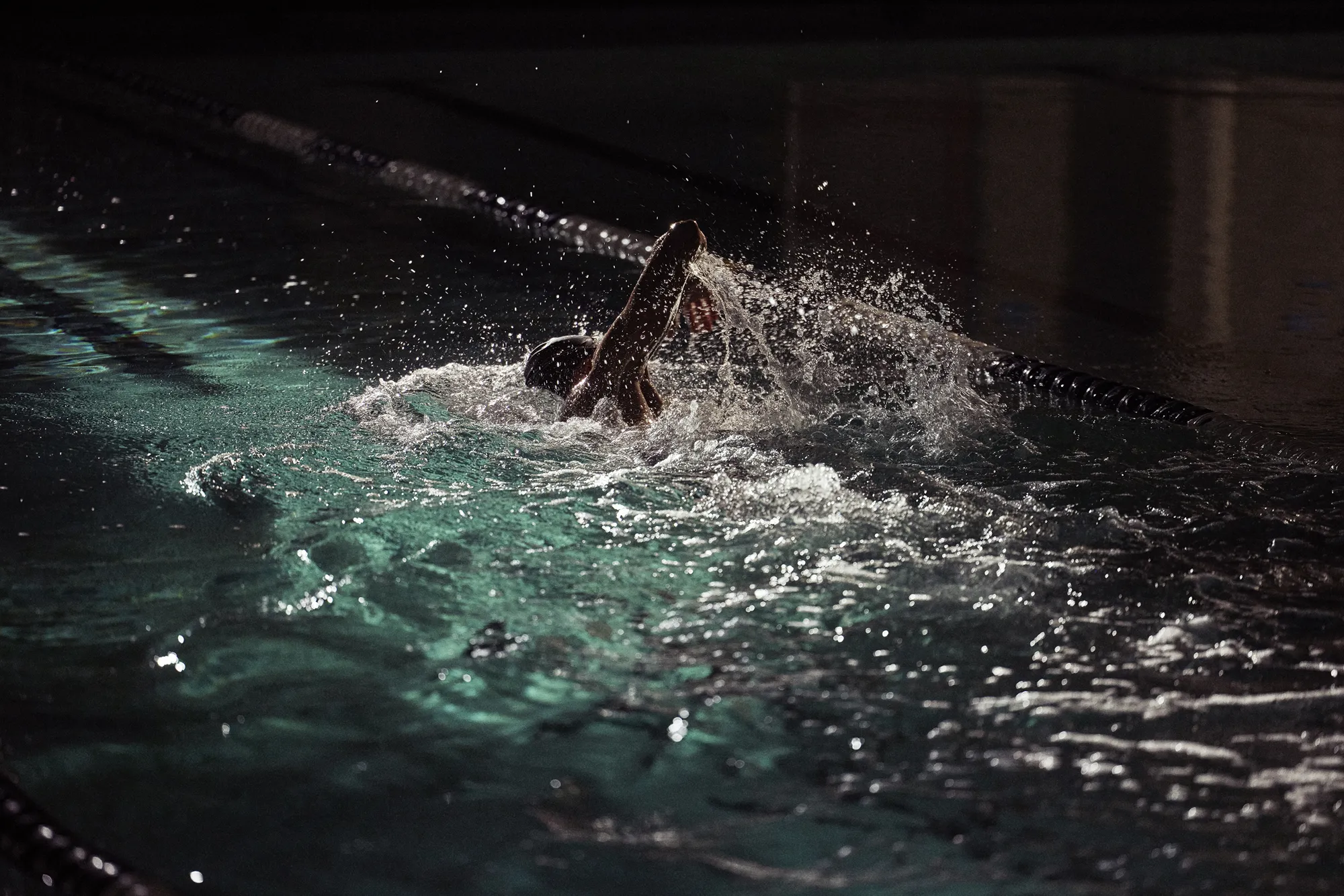 Man swimming freestyle laps in a dark indoor pool