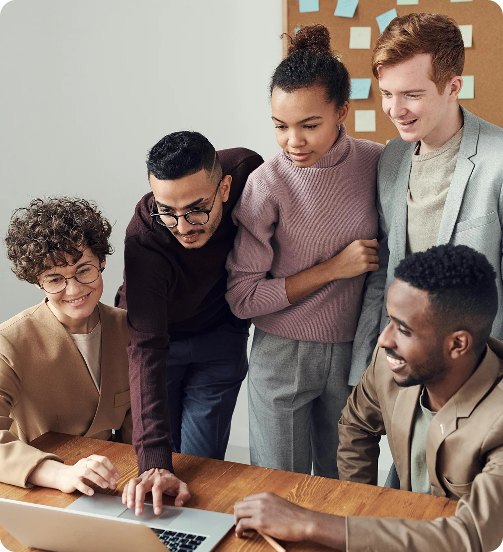 Five diverse young professionals gathered around a laptop, collaborating and smiling in a modern office.
