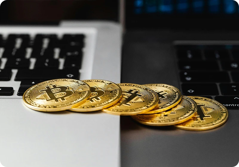 Stack of gold Bitcoin coins resting on the edge between two laptop keyboards, one silver and one black.