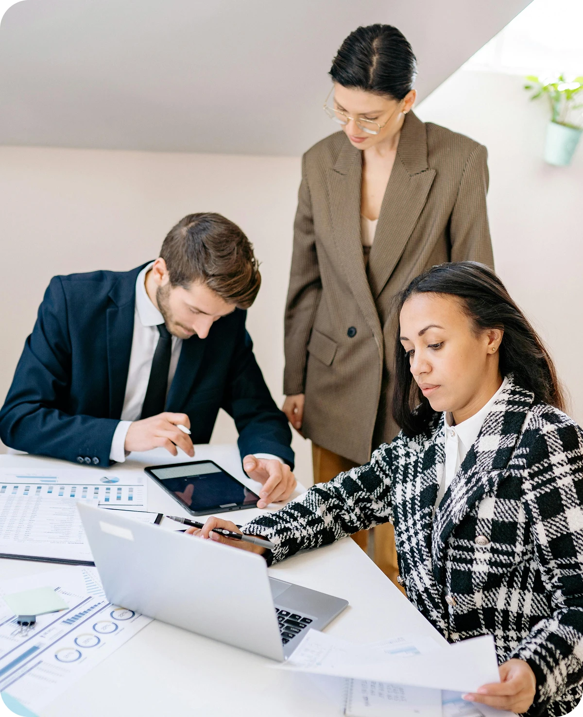 Three professionals working together at a desk with laptop, tablet, and documents in a modern office.