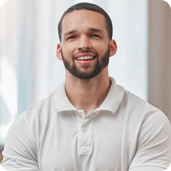 Smiling man with short hair and beard wearing a white polo shirt against a blurred light background.