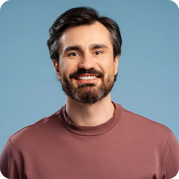 Smiling man with dark hair and beard wearing a maroon shirt against a blue background.