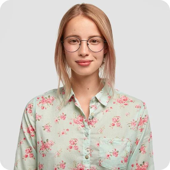 Smiling young woman with glasses wearing a light green floral button-up shirt against a plain background.