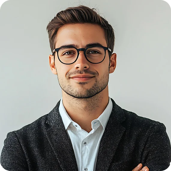 Young man with short brown hair, glasses, and a trimmed beard wearing a white shirt and dark blazer, smiling with arms crossed.