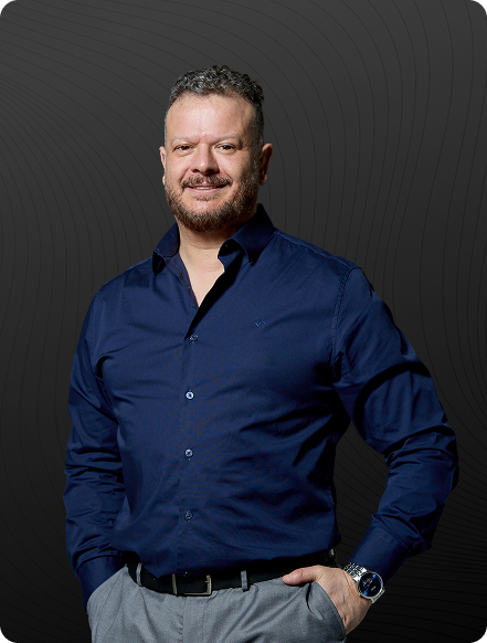 Homem vestido com terno cinza escuro e camisa azul, com barba e cabelo curto, posando sentado.
