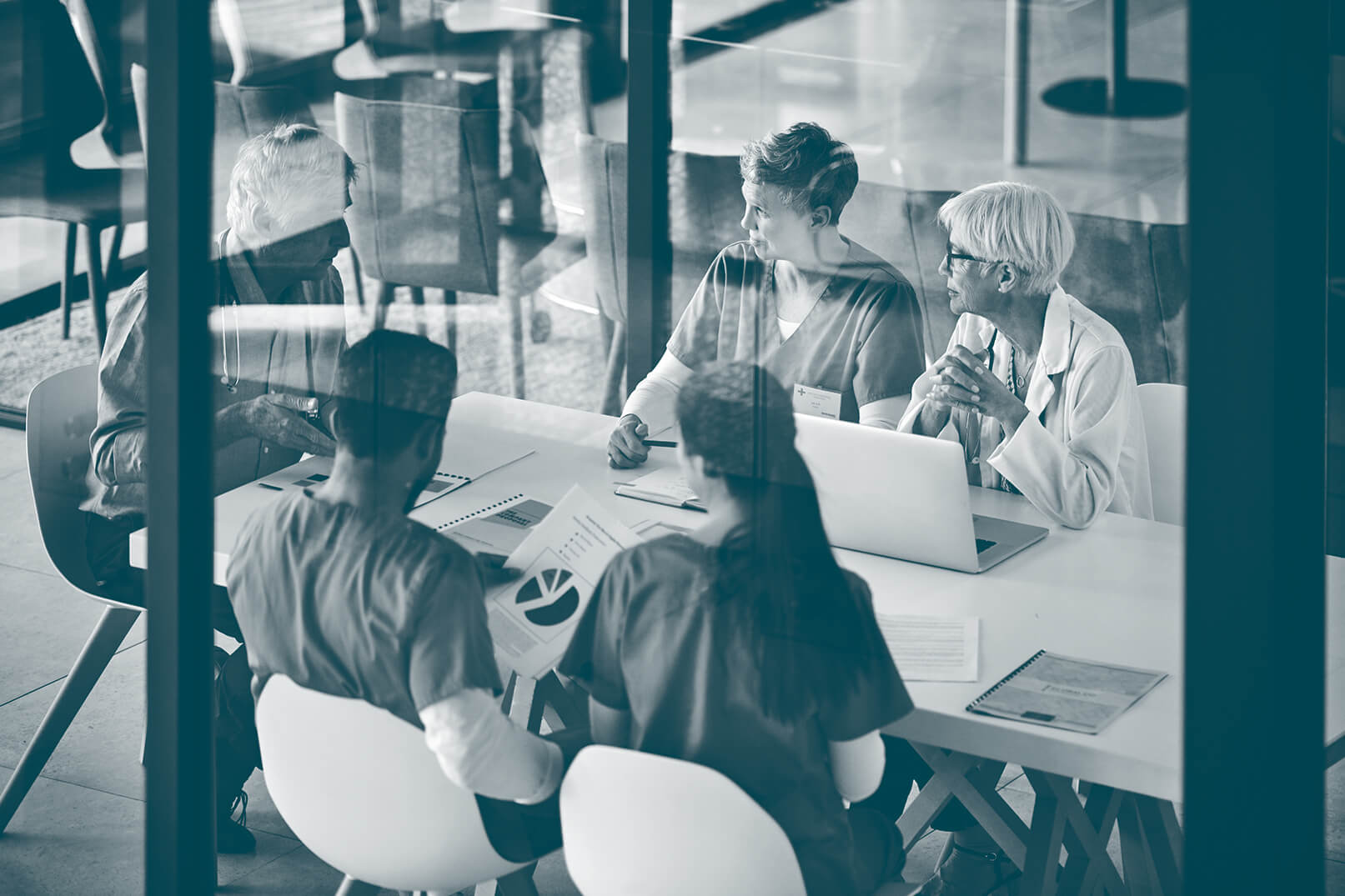 Medical professionals and healthcare workers in a meeting around a table with documents and a laptop.