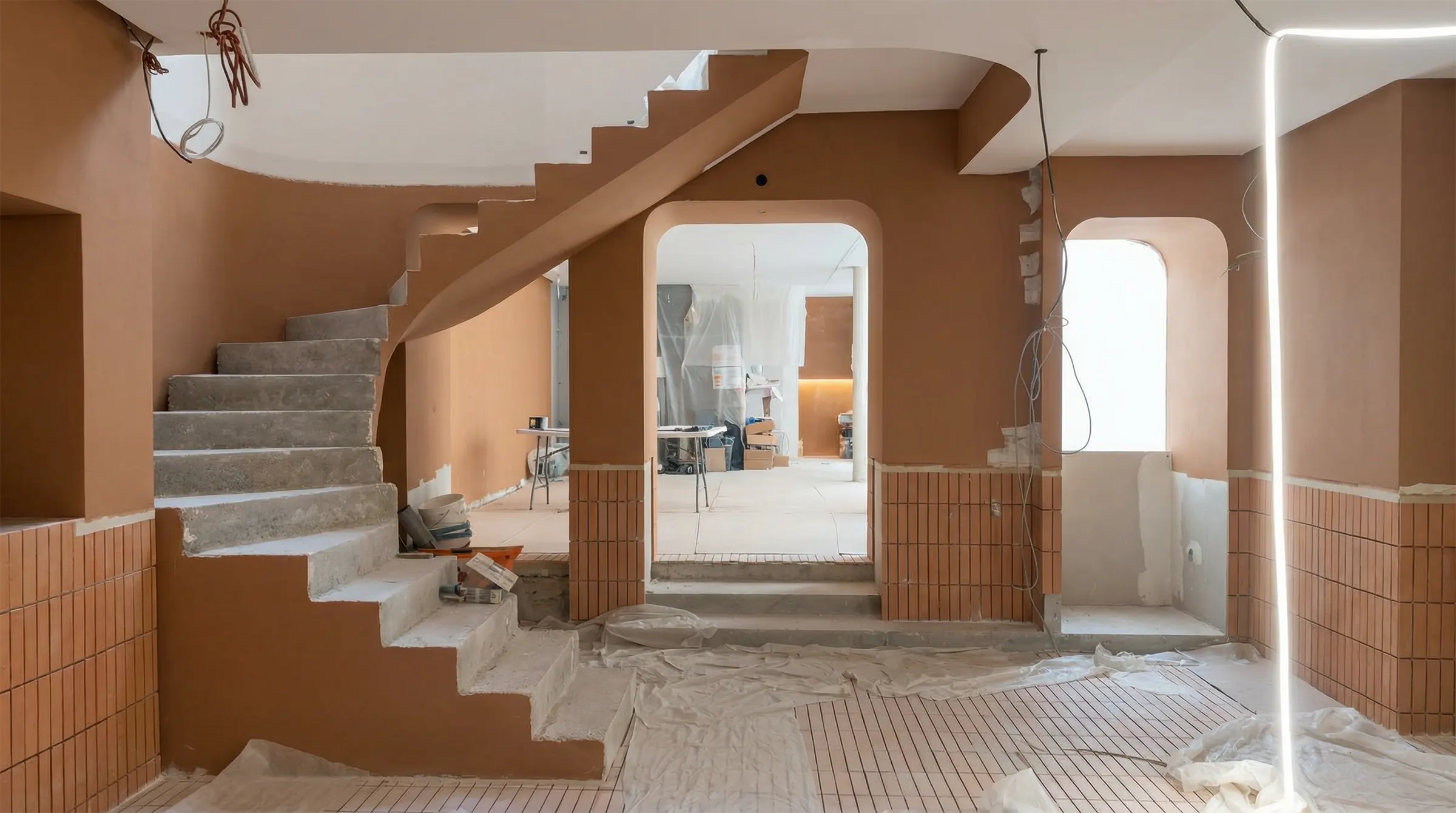 Intérieur en cours de rénovation avec un escalier en béton, murs orange avec carreaux bas, et matériel de chantier.
