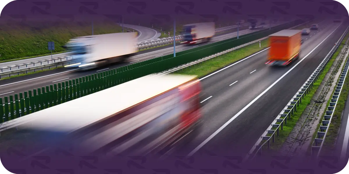 Trucks blurred by motion as they travel in both directions on a divided multi-lane highway.