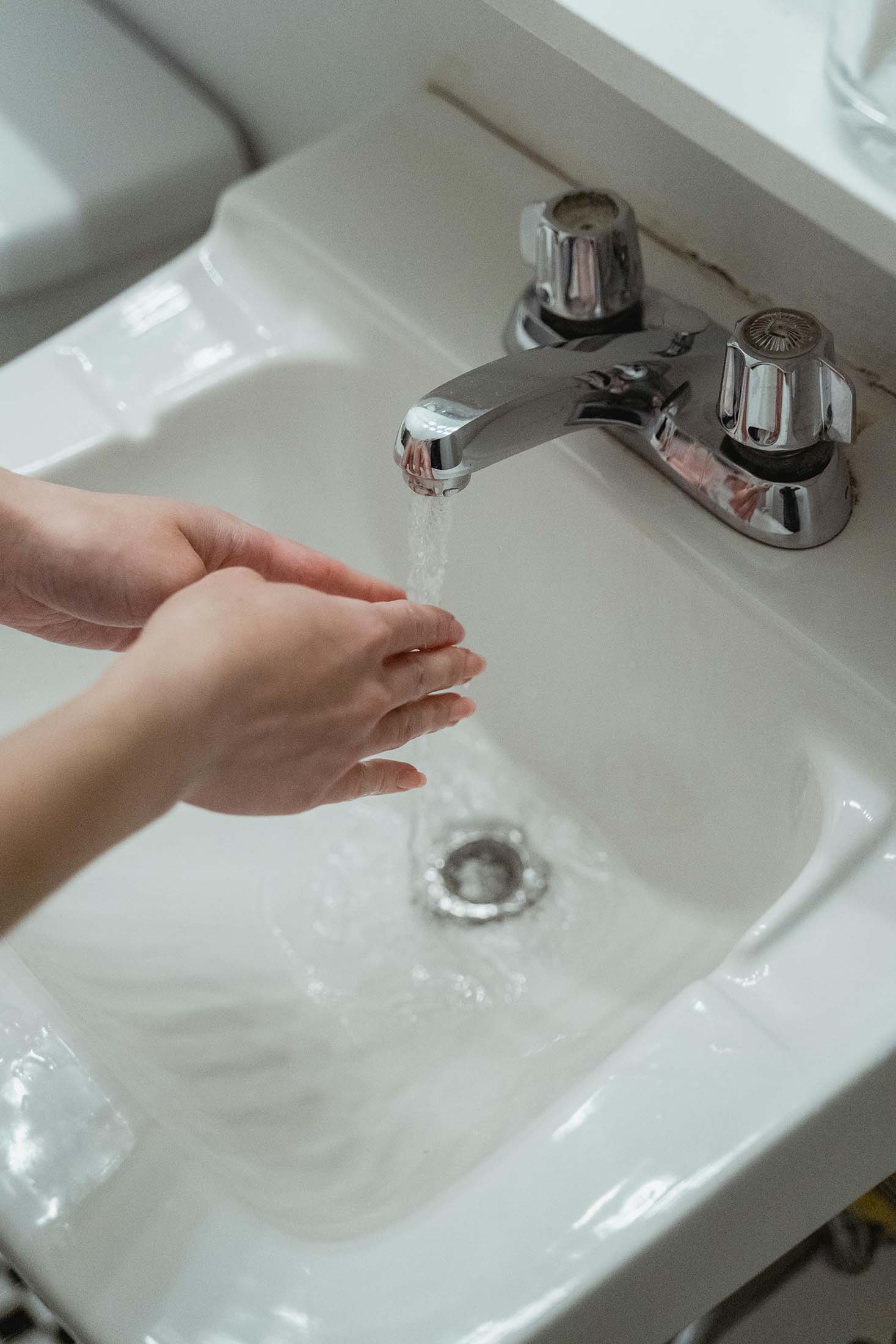 Person washing hands under running water from a chrome faucet in a white sink.
