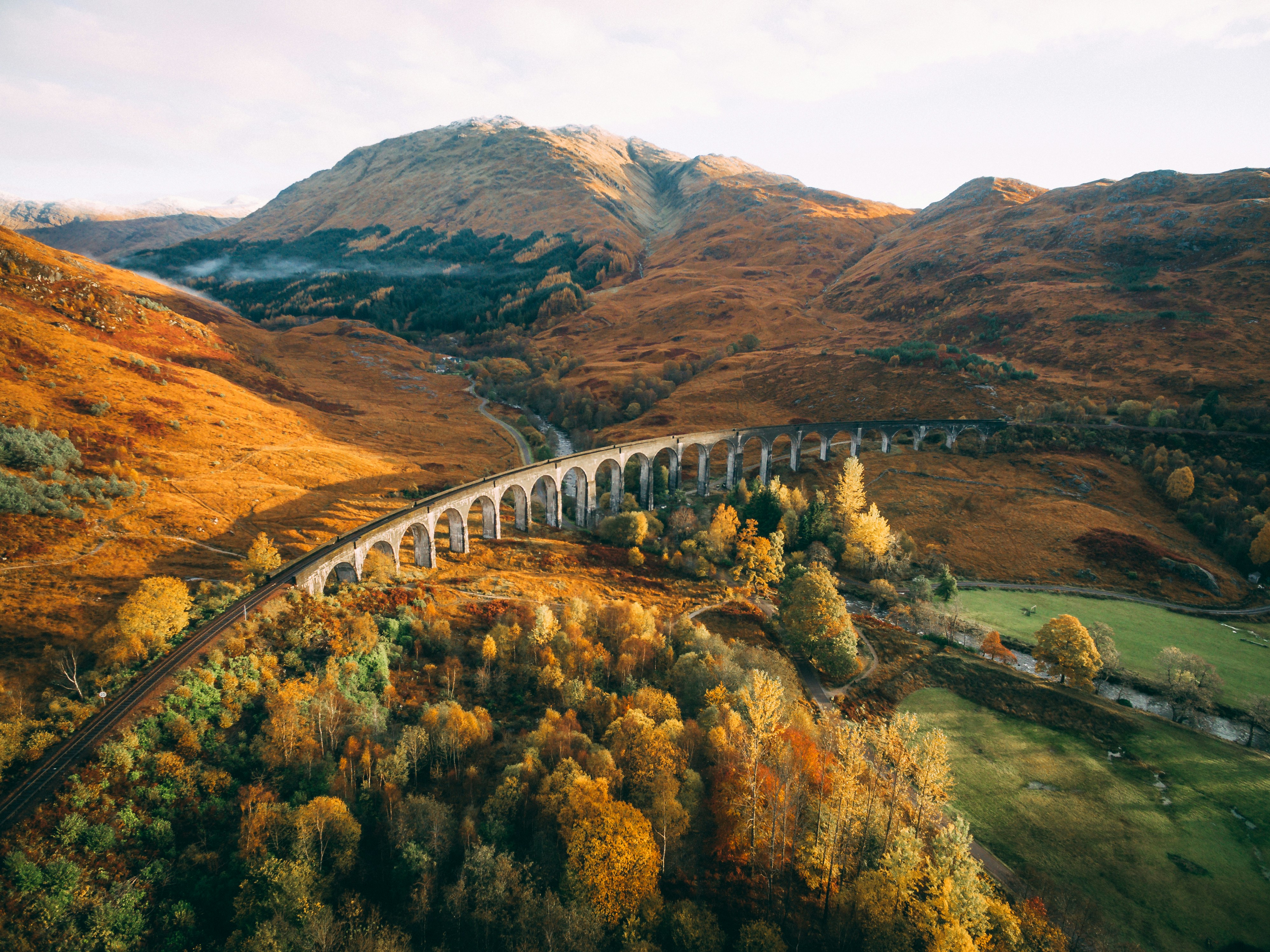 Curved stone railway viaduct crossing autumn-colored hills and trees in a mountainous landscape.
