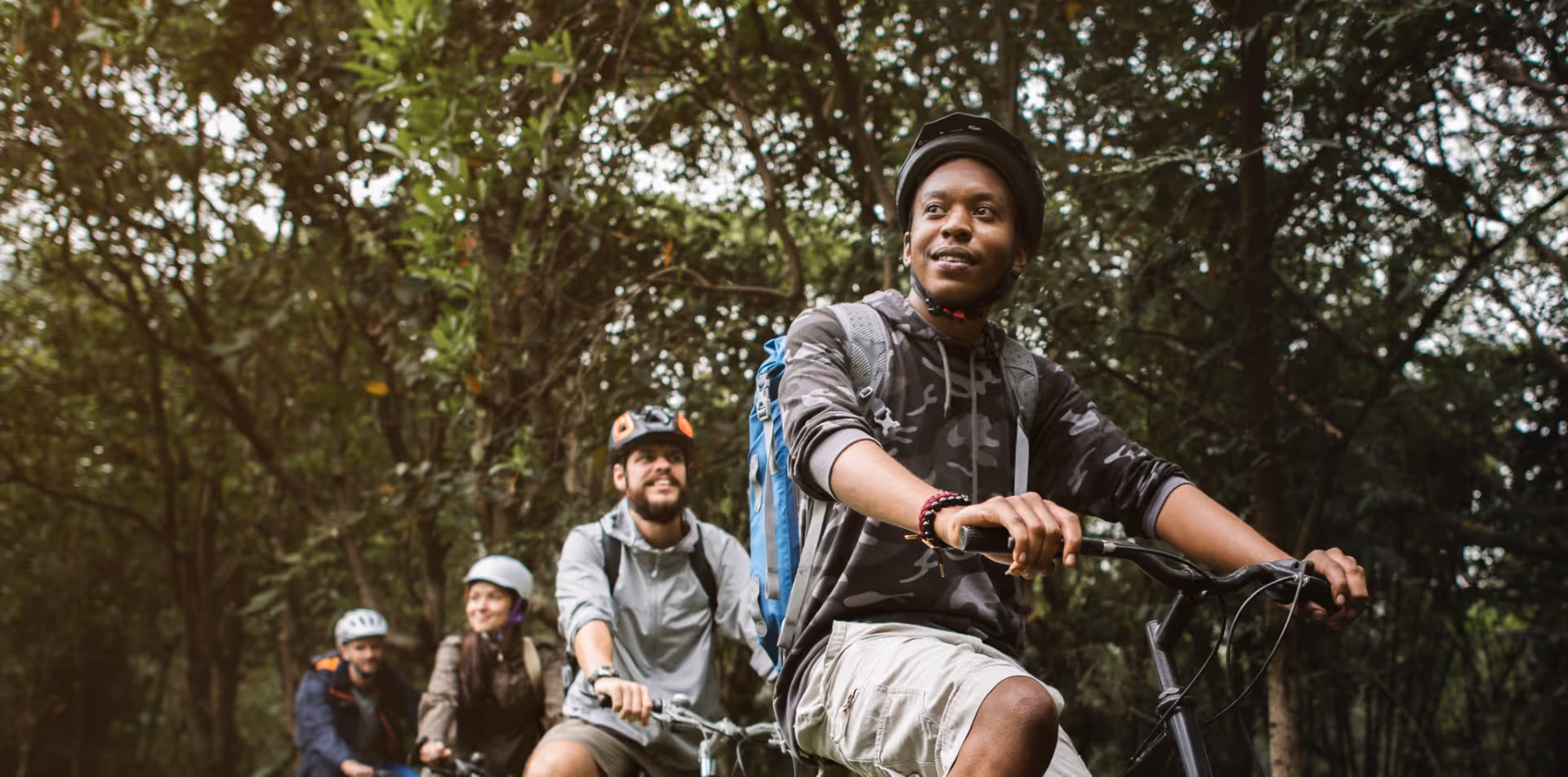 Mountain bikers riding through forest trail with helmets and backpacks