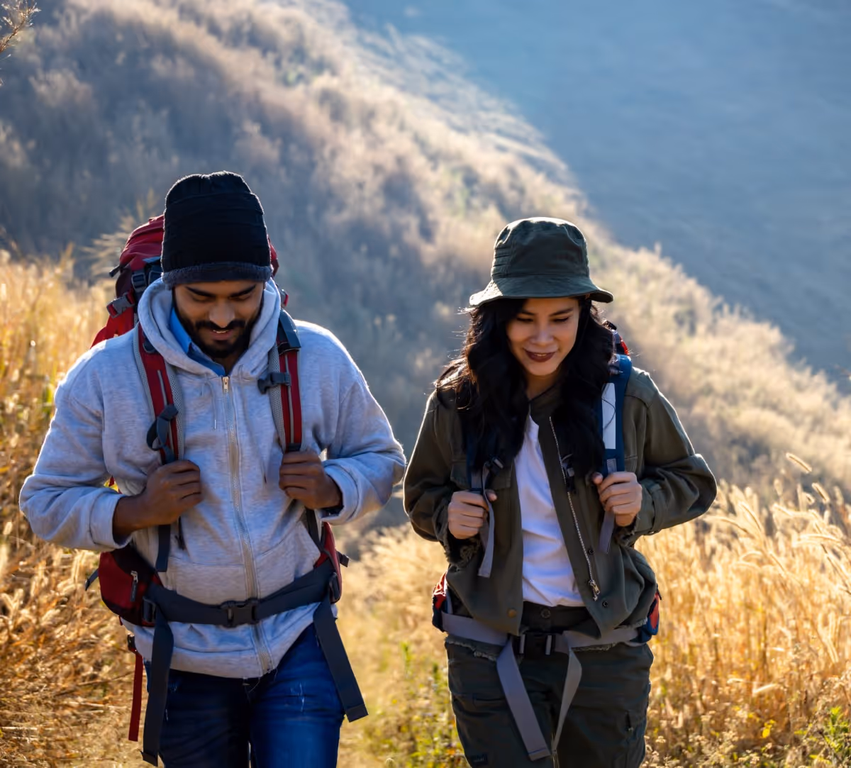 Two hikers walking on mountain trail with backpacks on sunny day