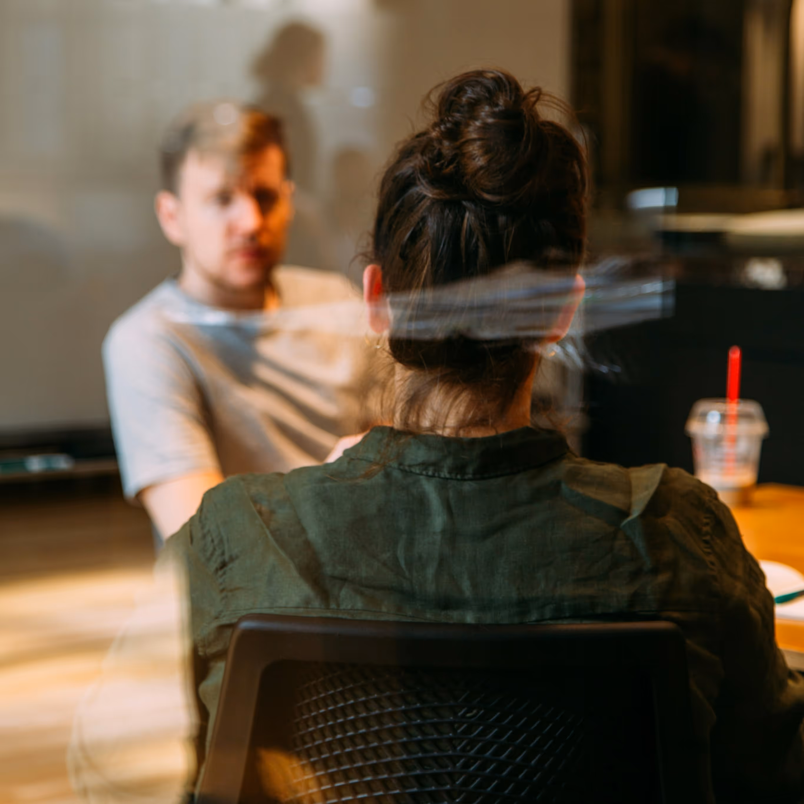 Two people sitting at a table, one from behind with hair in a bun