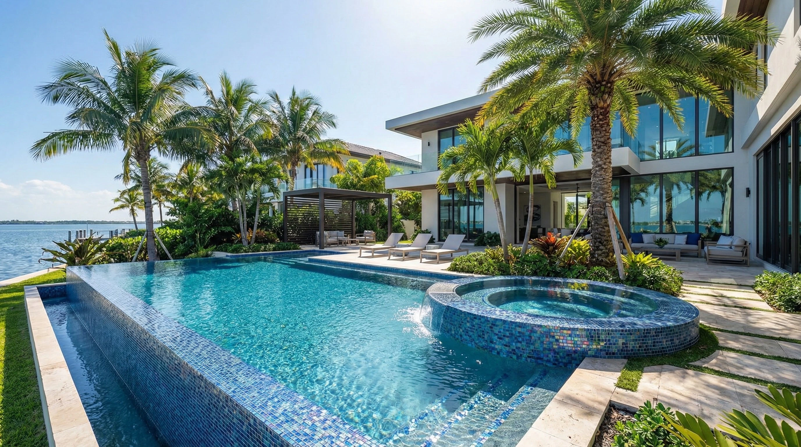 Luxury pool design in Florida featuring a modern infinity-edge pool with glass tiles, integrated spa, and tropical landscaping designed for upscale outdoor living.