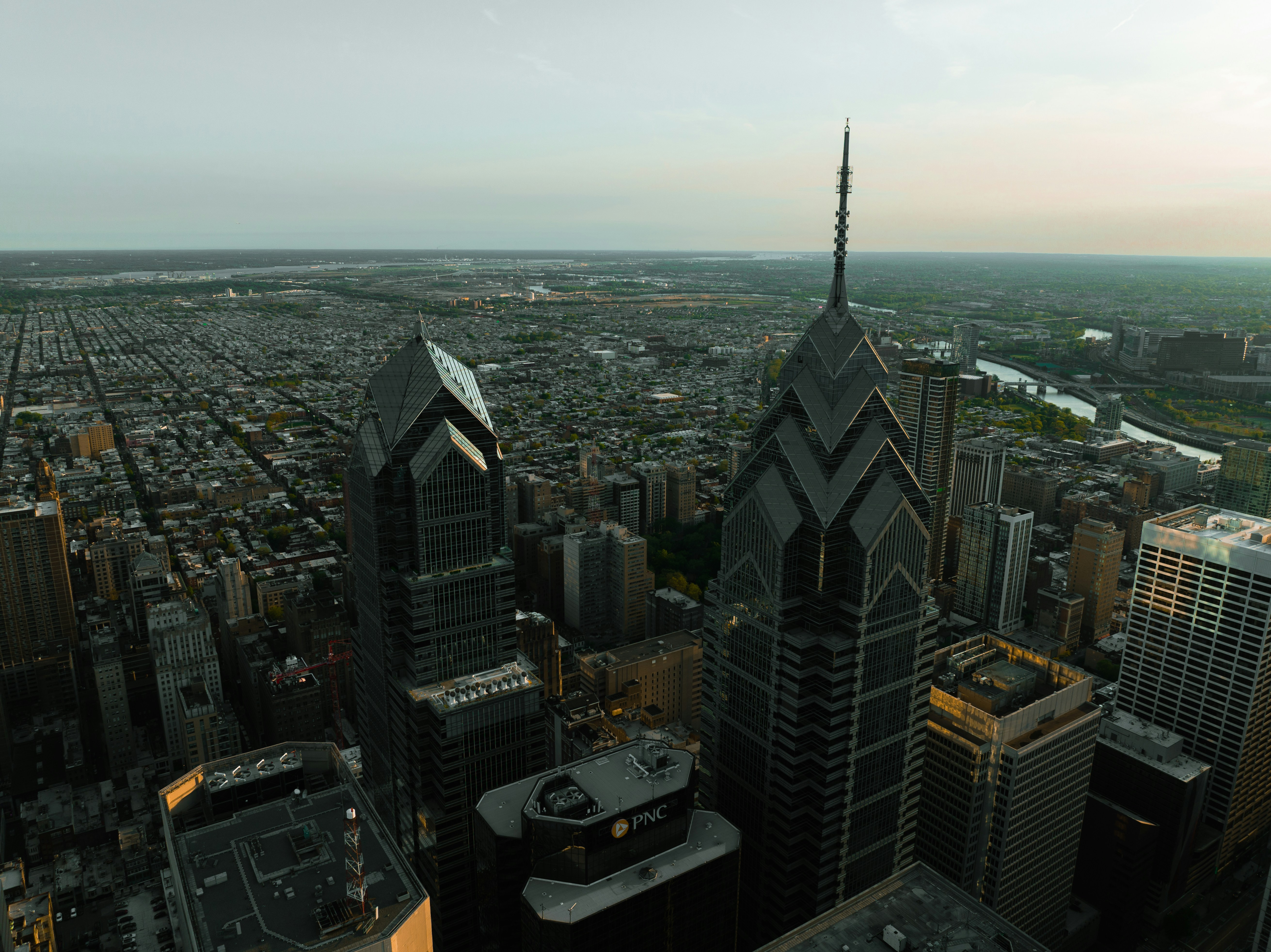 Aerial view of city skyscrapers with a river and sprawling urban landscape in the background at dusk.