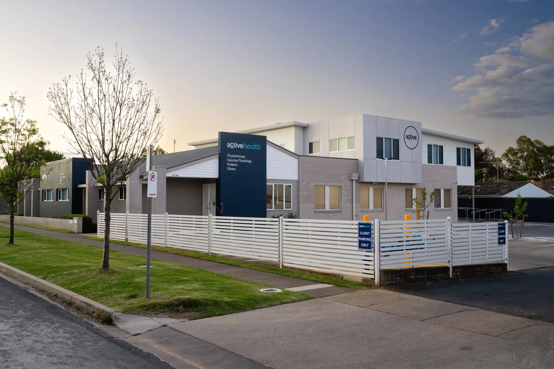 Modern single-story medical building with Active Health signage and fenced client parking on a quiet street.