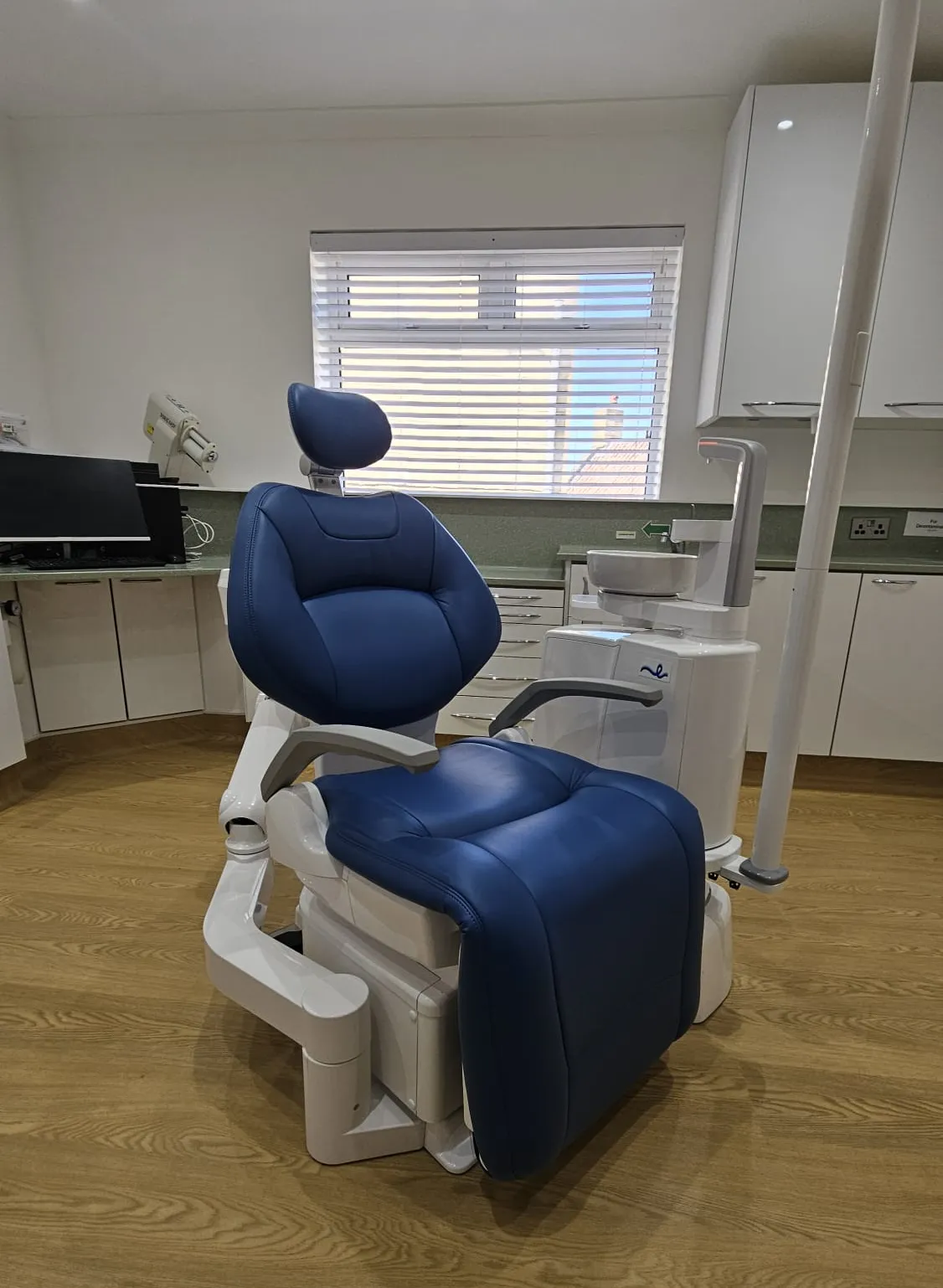Modern dental chair with blue upholstery in a clean dental office with wooden floor and white cabinets.