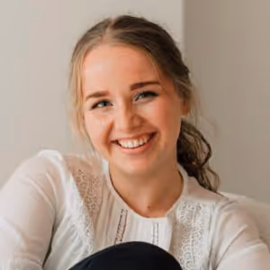 Jonge vrouw met een lichte blouse die glimlacht en haar haar in een losse paardenstaart draagt.