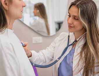 Female doctor uses a stethoscope to check a patient's heartbeat in a medical office.