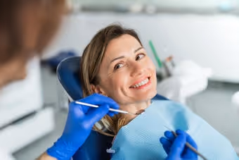 Smiling woman reclined in dental chair during dental checkup with dentist wearing blue gloves.
