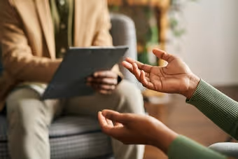 Close-up of two people talking, one holding a clipboard, the other gesturing with hands.