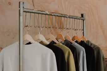 Metal clothing rack with hangers holding various neutral-toned shirts and jackets.