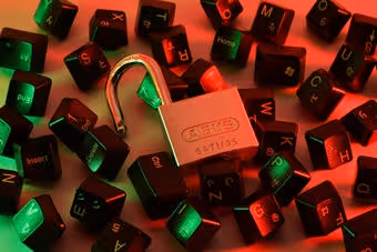 Unlocked silver padlock on scattered black keyboard keys with red and green lighting.