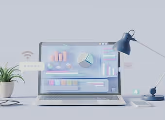 Laptop on desk showing colorful 3D charts and graphs with a desk lamp and plant beside it.