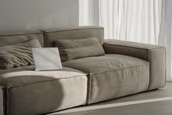Gray sofa with cushions and closed laptop near white curtains in soft natural light.