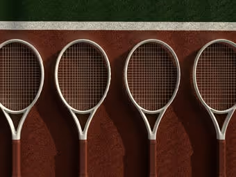 Four tennis rackets lined up vertically on a red clay tennis court near the green boundary line.