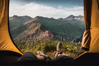 View of mountains and wildflowers outside a tent with legs and hiking boots visible inside.