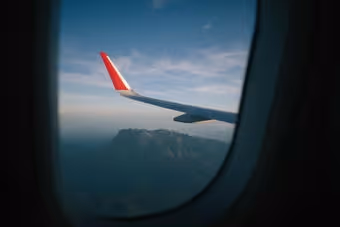 View of an airplane wing with a red tip over mountains seen through a plane window.
