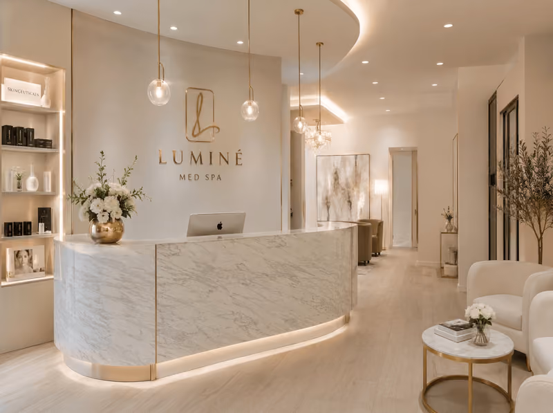 Modern spa reception with marble desk, pendant lights, branding sign, and cozy seating area with plants.