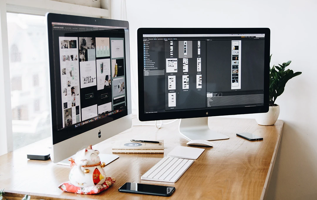 Two computers on a desk with design software displays