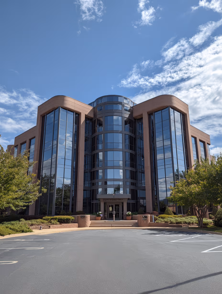 Modern office building with large reflective glass windows under a partly cloudy blue sky.
