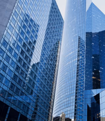 Cluster of tall modern glass skyscrapers reflecting the blue sky and nearby buildings.
