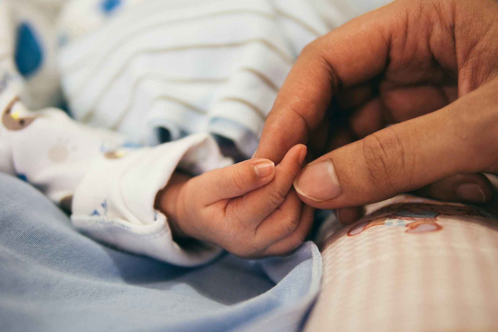 Hand eines Erwachsenen hält die Hand eines Neugeborenen während des Vaterschaftsurlaubs in der Schweiz