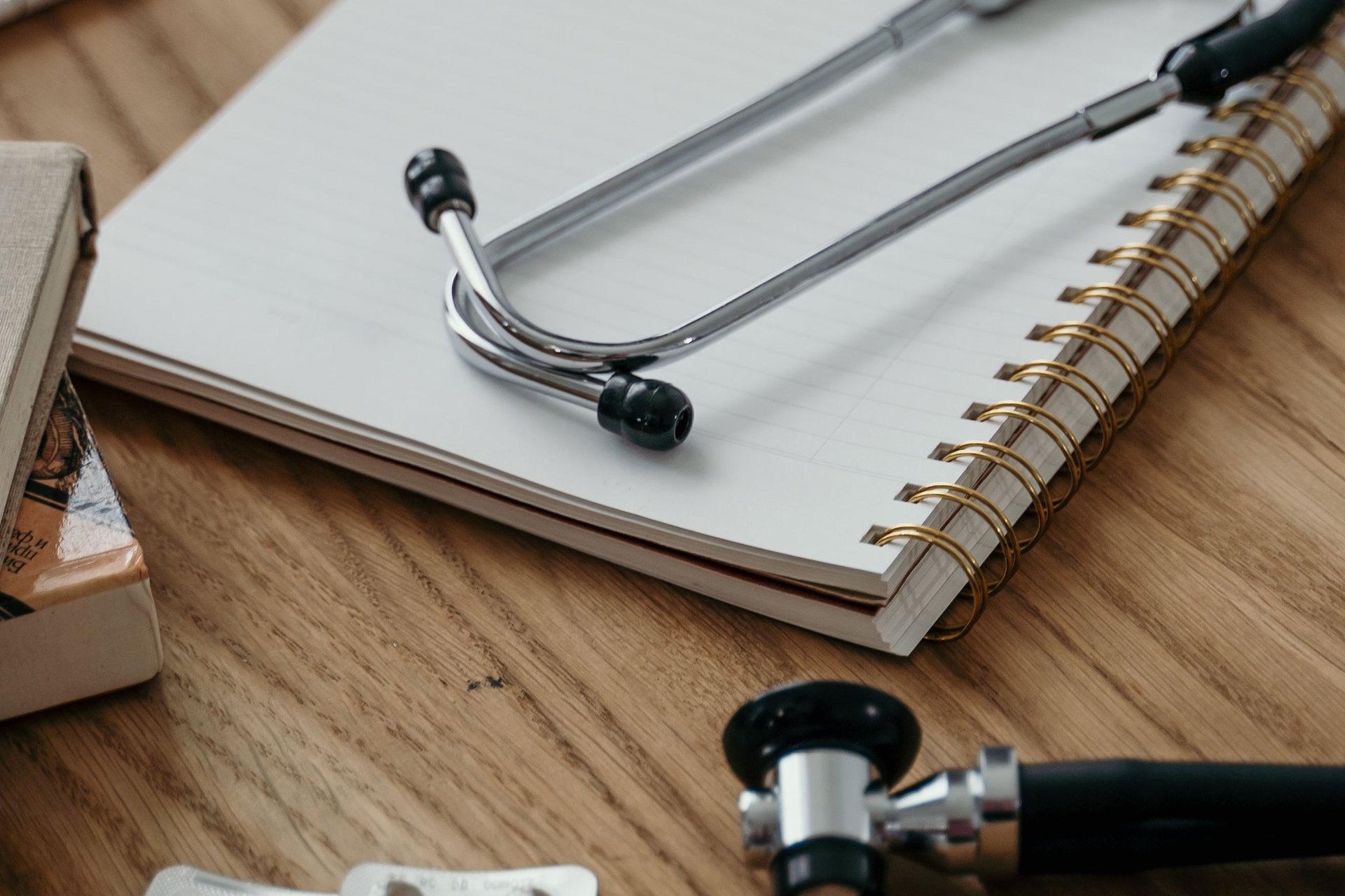 Un stéthoscope posé sur un carnet, sur un bureau en bois, comme lorsqu'un certificat médical arrive chez l'employeur pendant un arrêt maladie en Suisse