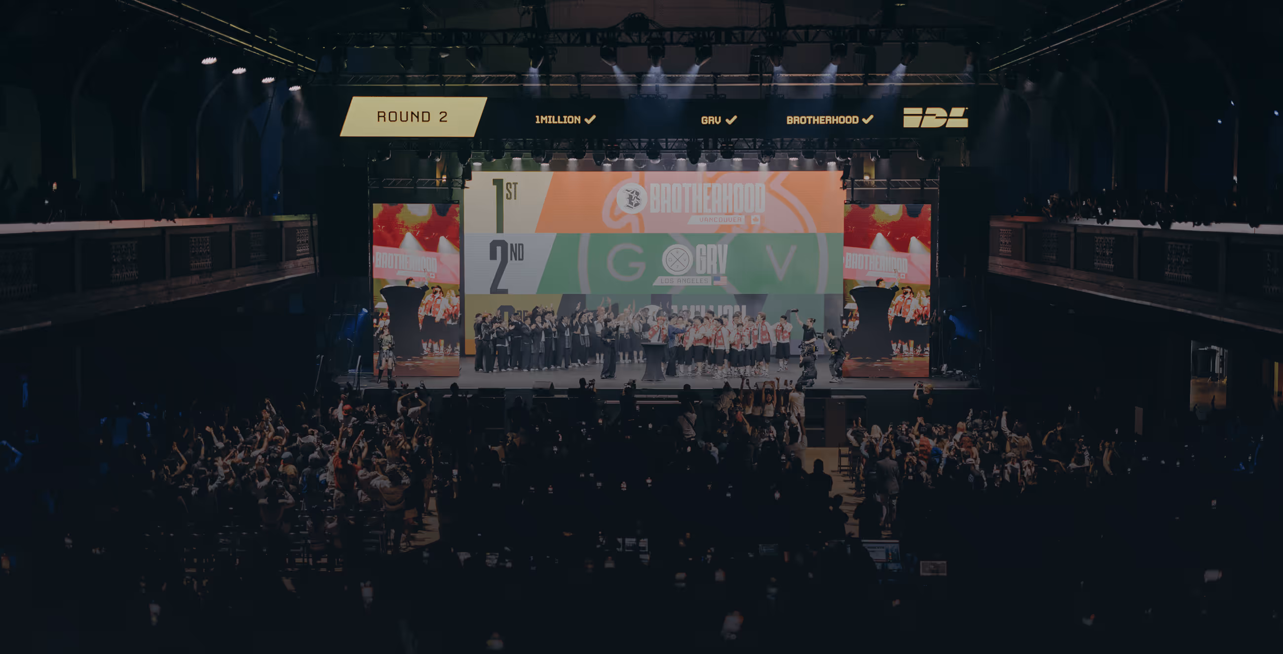 Large crowd watching a stage event with teams Brotherhood and GRV celebrating their standings in round 2 of a competition.