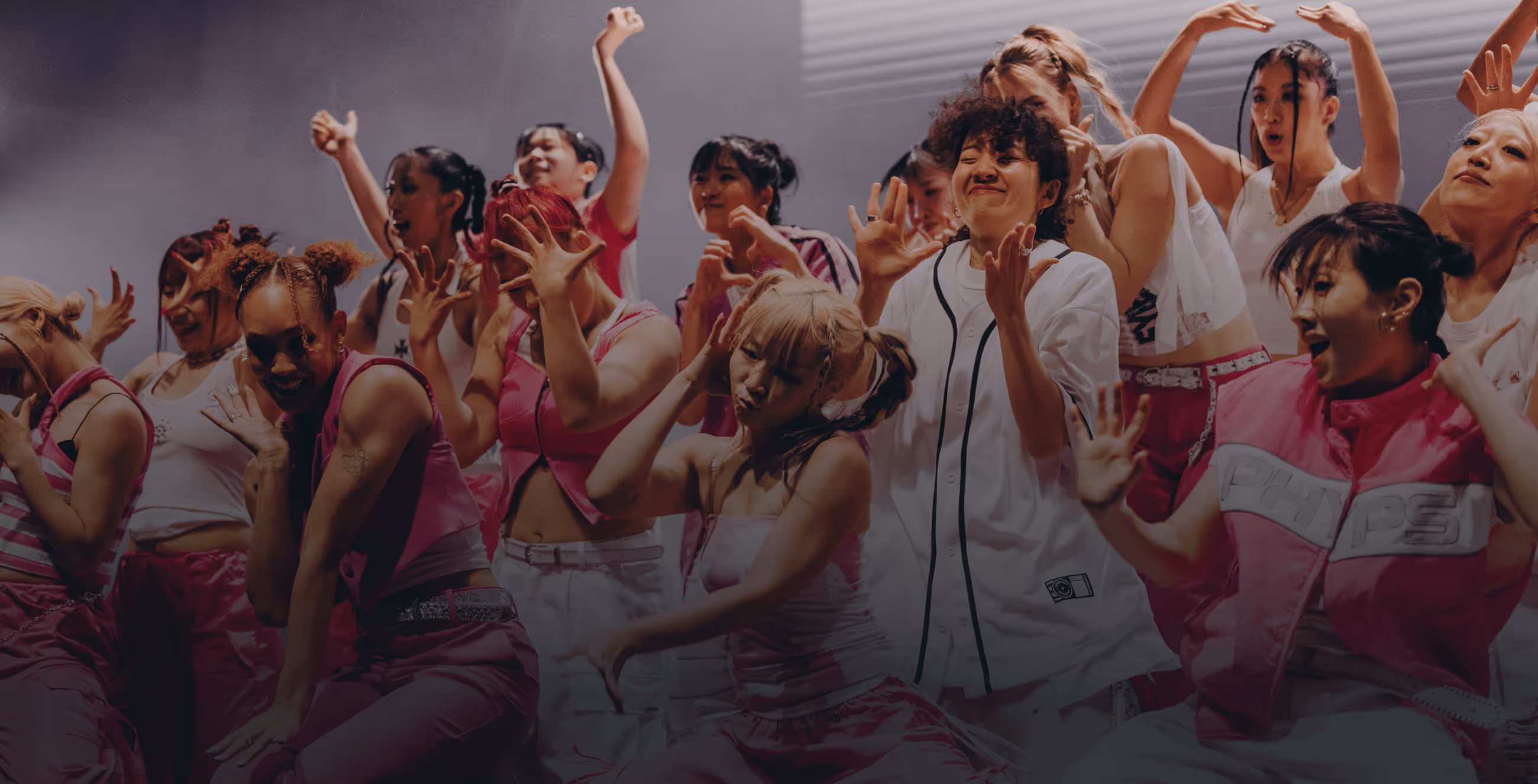 Group of diverse young women dancing energetically on stage wearing pink and white outfits.